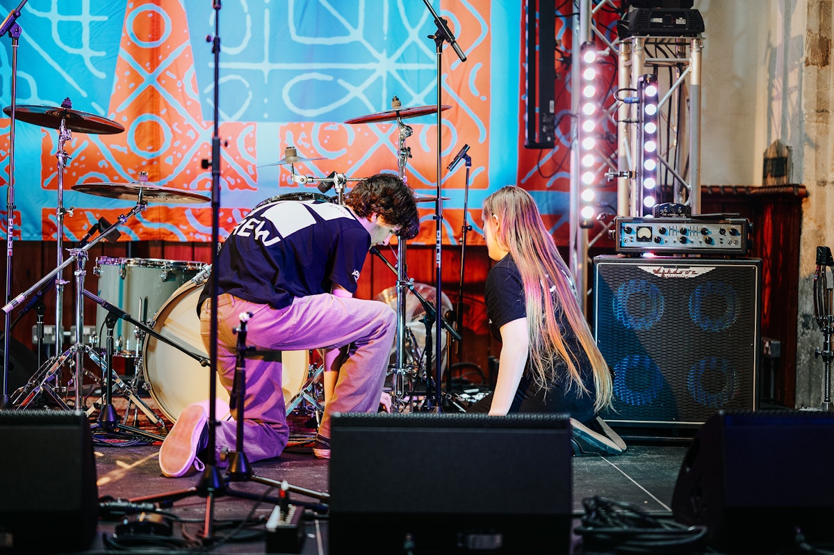 Two volunteers kneeling on stage adjusting drum equipment under colourful lighting at St Stephen’s church